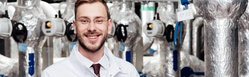 Preview: panoramic shot of happy bearded engineer in white coat near air compressed system