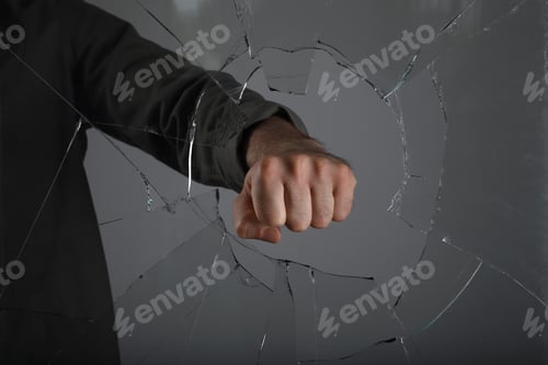 Preview: Man breaking window with fist on grey background, closeup