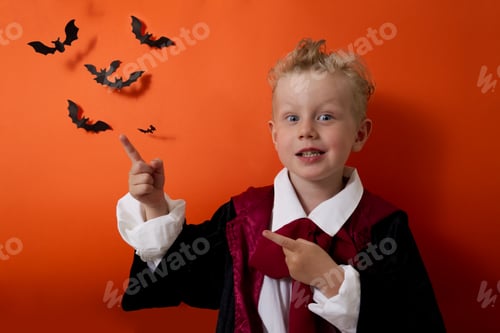 Preview: A boy in a vampire costume points to an empty space with his fingers on an orange background
