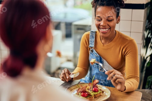 Preview: A smiling African woman having breakfast with her friends, smiling while taking a first bite.