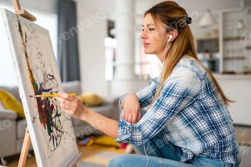 Preview: Happy young woman paints on canvas at home