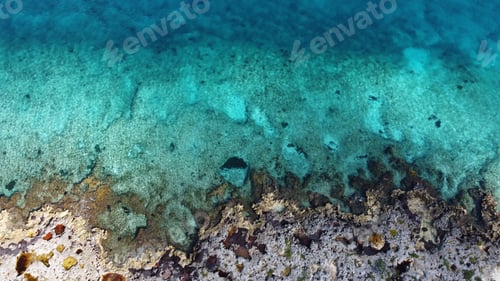 Preview: Aerial shot of a turquoise sea meeting the rocky shore during daytime