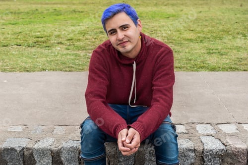 Preview: Portrait of a young man with blue hair looking at camera outdoors