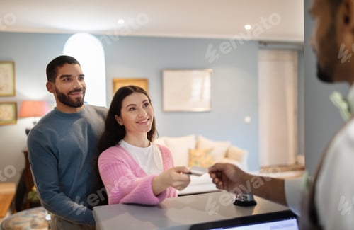 Preview: Couple Checking At Hotel Giving Credit Card To Receptionist Indoors
