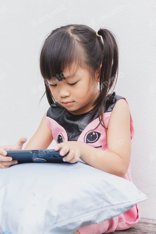 Visualização: Menina criança asiática feliz assistindo e usando telefone inteligente. Inclinando-se e usando tecnologia, mídias sociais.