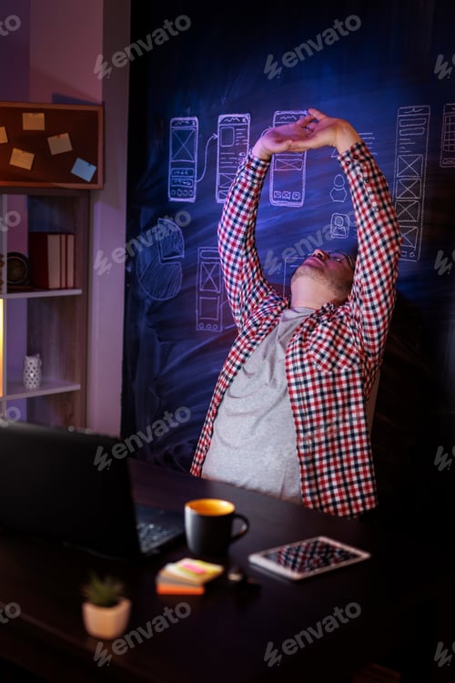 Preview: Man stretching out while working late in home office