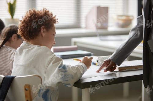 Visualização: Menino pré-adolescente recebendo orientação do professor enquanto estuda em sala de aula