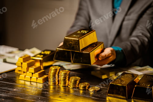 Preview: A businessman sits at his desk in a nighttime office, using a laptop to analyze gold bar prices