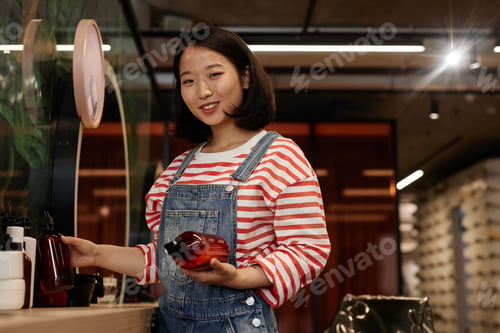 Preview: Smiling Asian Hairstylist in Beauty Salon Holding Shampoo Bottles