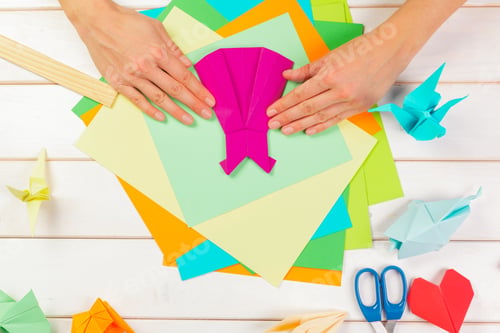 Preview: Hands working on colorful paper for origami designs in a crafting space