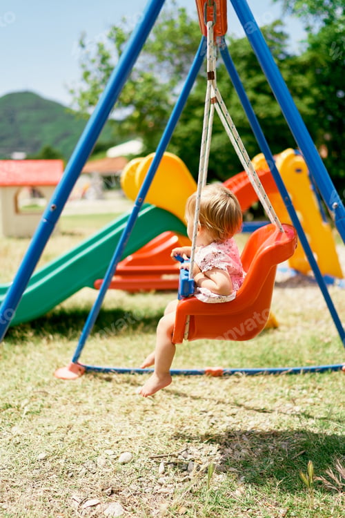 Preview: Little girl sits on a swing in the park. Side view
