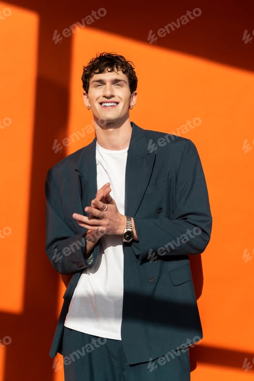 Preview: Smiling man in stylish outfit looking at camera on orange background with sunlight