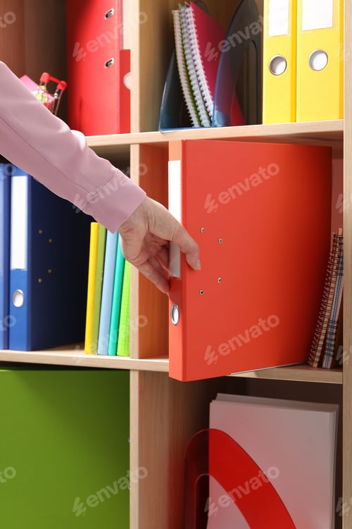Preview: Woman taking binder office folder from shelving unit, closeup