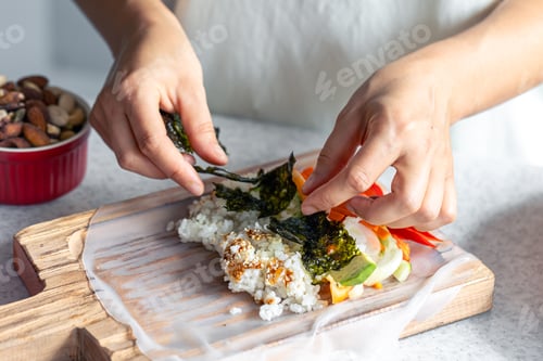 Preview: Woman preparing spring rolls in rice paper on kitchen table.