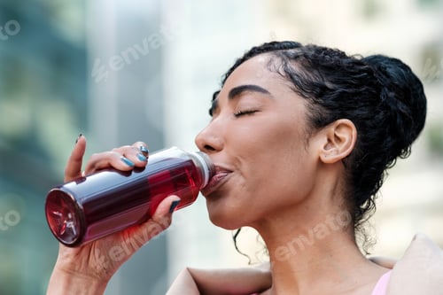 Preview: Headshot of fitness young woman drinking energy drink outdoors.