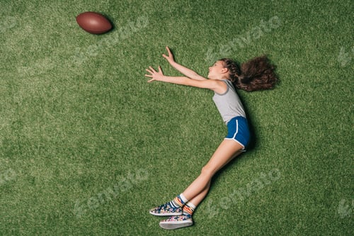 Preview: top view of little sportive girl catching rugby ball on grass, athletics children concept