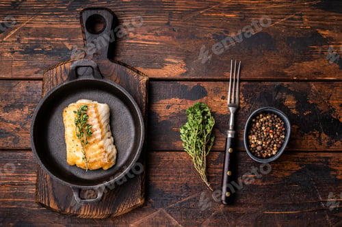 Preview: Roasted cod fish loin fiilet in skillet. Wooden background. top view