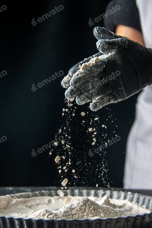 Preview: front view female cook pouring white flour into the pan with her palms on dark background egg cake