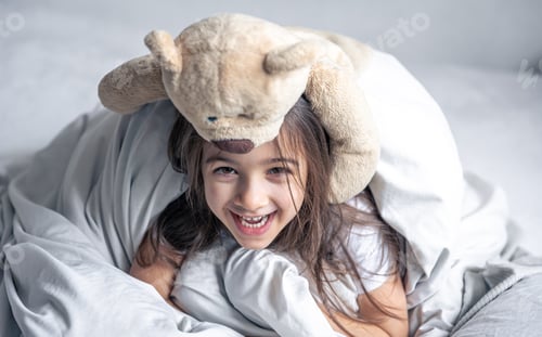 Preview: Little cute girl in bed with a teddy bear early in the morning.