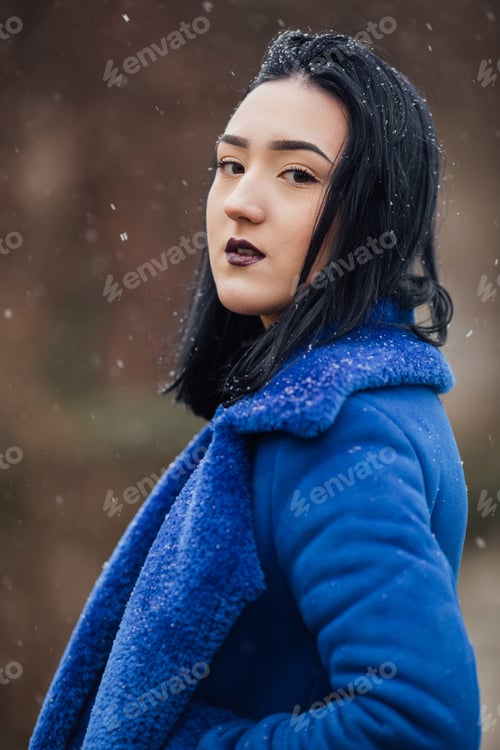 Preview: Vertical shot of a young brunette female with dark lipstick posing in a warm blue jacket