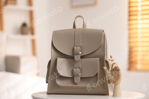Preview: Stylish beige backpack and wooden mannequin hand on white table indoors