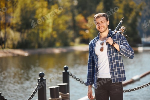 Preview: young fisherman with rod and sunglasses fishing in lake