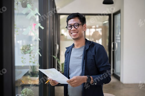 Preview: Young creative man standing in modern office and smiling to camera.