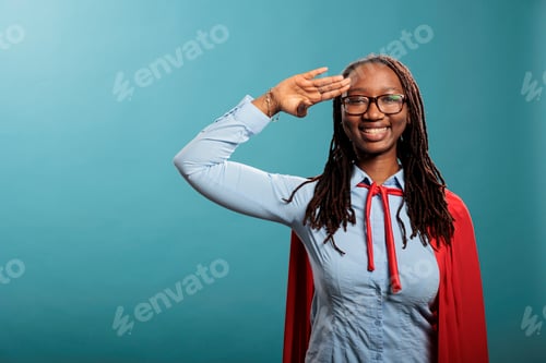 Preview: Brave and proud happy smiling superhero woman wearing mighty hero cape while making soldier salute