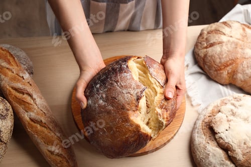 Preview: Woman breaking freshly baked bread at wooden table, closeup