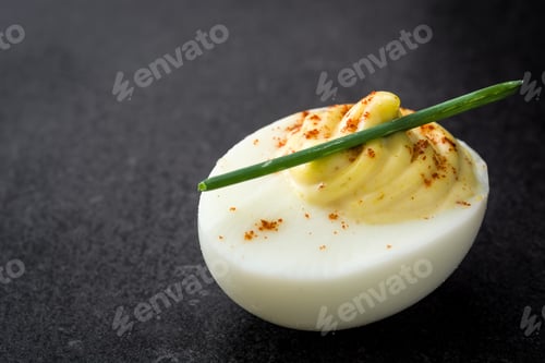 Preview: Delicious deviled egg garnished with paprika and chive on dark background