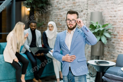 Preview: Business and team working concept. Handsome young businessman in suit putting on his eyeglasses