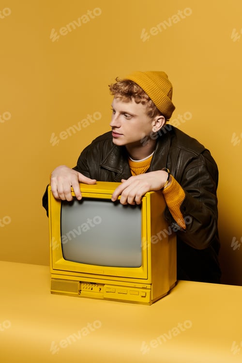 Preview: A young redhead man showcases a fashionable winter outfit leaning on a retro TV