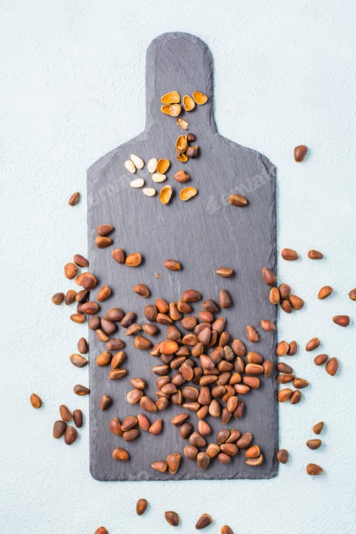 Preview: Several peeled pine nuts among in-shell nuts on a slate board. Remedy for insomnia and detox food.