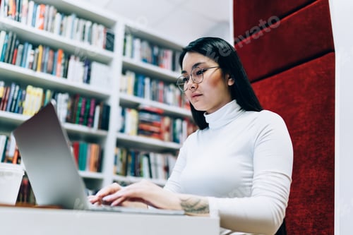 Preview: Serious Asian woman typing on laptop in library