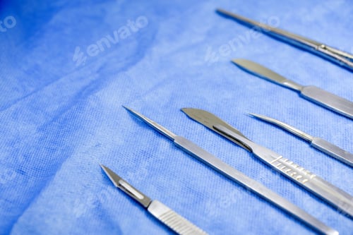 Preview: High angle shot of sterile scalpels on a blue surface under the lights