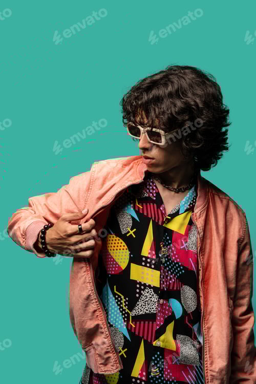 Preview: Happy young ethnic man with pink jacket standing at turquoise backdrop