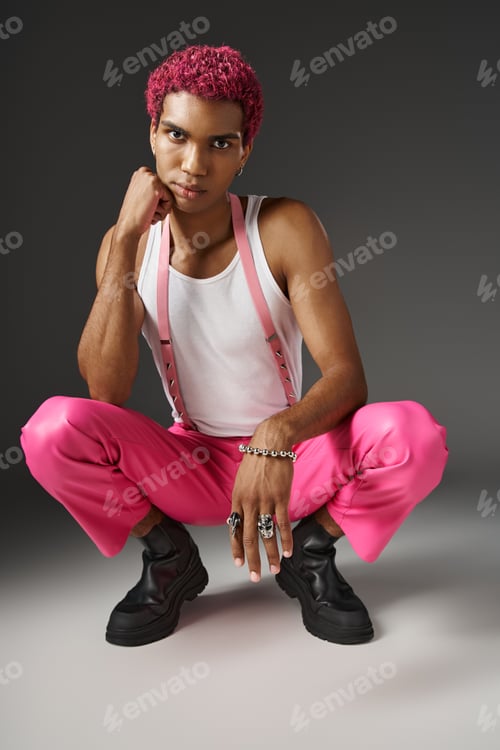 Preview: trendy african american man posing on gray backdrop squatting and looking at camera, fashion concept
