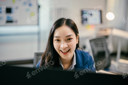 Preview: Young businesswoman smiling and working on her computer in a modern office, focused and cheerful