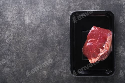Preview: Beef steak. Fresh raw beef steak with fork and rosemary in vacuum black plastic pack on black stone