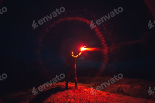 Preview: The man with a red firework stick standing on a mountain. evening night time.
