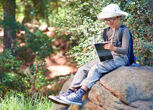 Preview: Reading up on owls. A little boy with a book in his hand sitting on a rock.
