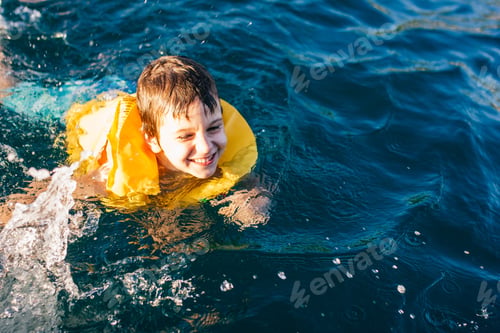Preview: cheerful boy in a life jacket swims in the sea