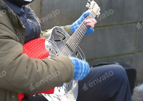 Preview: An unrecognizable street guitarist musician plays music with a band outside on a cold day in winter