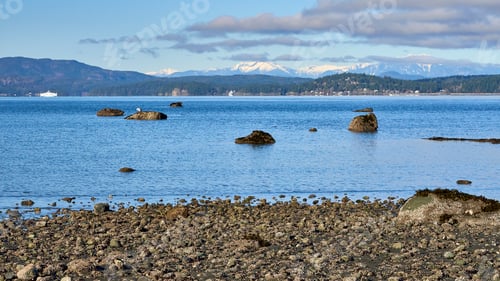 Preview: View from a rocky ocean beach of the beautiful blue ocean, two distant ferries and snowy mountains.