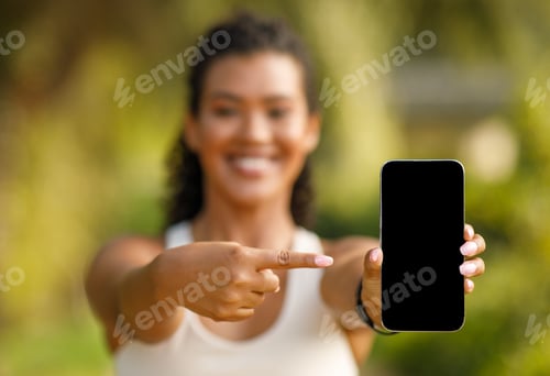 Preview: fitness woman in sportswear pointing at blank phone screen outdoors
