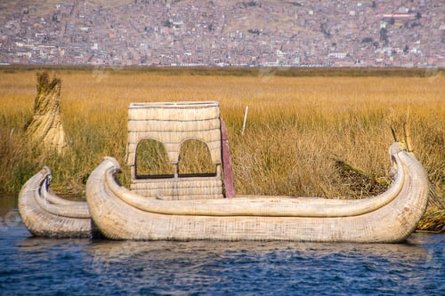 Preview: Wooden outriggers on the water by the grass covered field with a city in the background