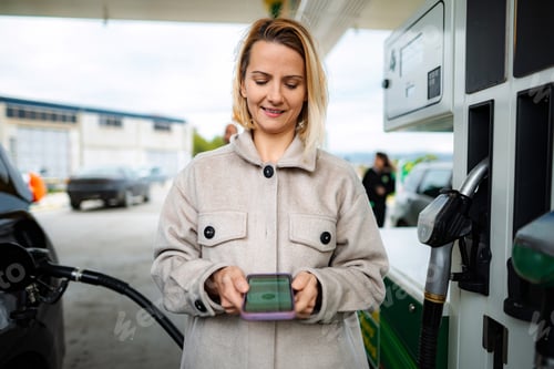 Preview: Woman paying for fuel with smartphone at gas station