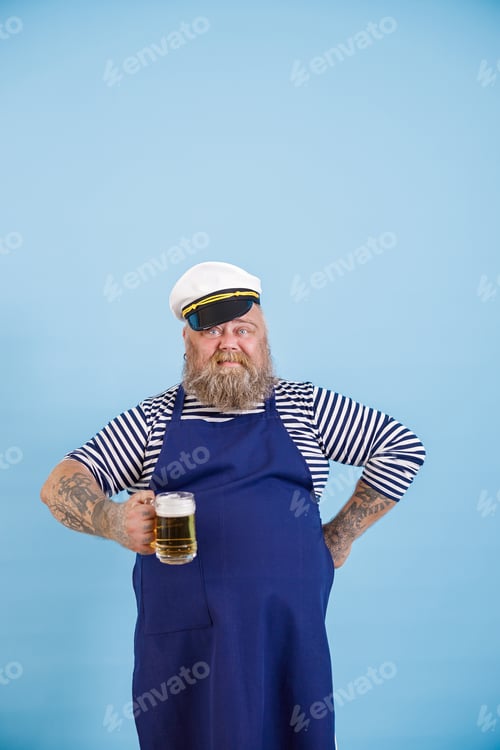 Preview: Confident man with overweight in sailor suit holds mug of tasty beer on light blue background