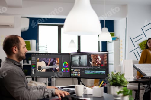 Preview: Videographer editing, cuting footage and sound on computer with dual monitors