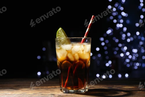 Preview: Glass with cola, lime slice and tubule against blurred lights background